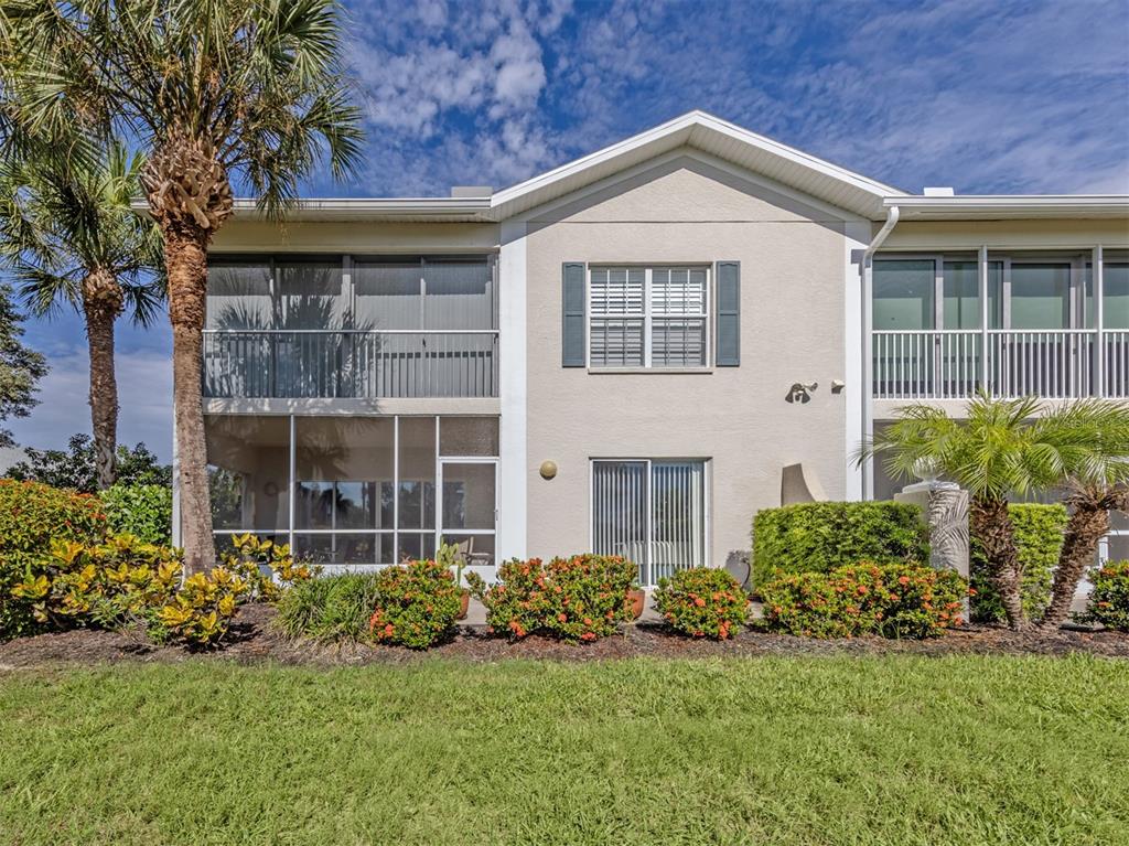 The exterior of a two-story residential building features screened balconies, sliding glass doors, and landscaping — 872 SARANAC LAKE DRIVE UNIT 106, VENICE, FL