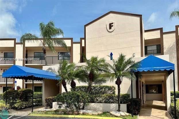 Exterior view of a multi-story apartment building with blue awnings and palm trees — TAMARAC, FL