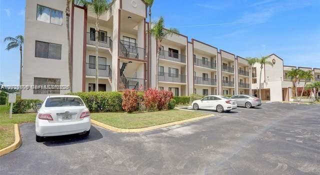 A multi-story apartment building with beige stucco walls and palm trees in a parking lot — TAMARAC, FL