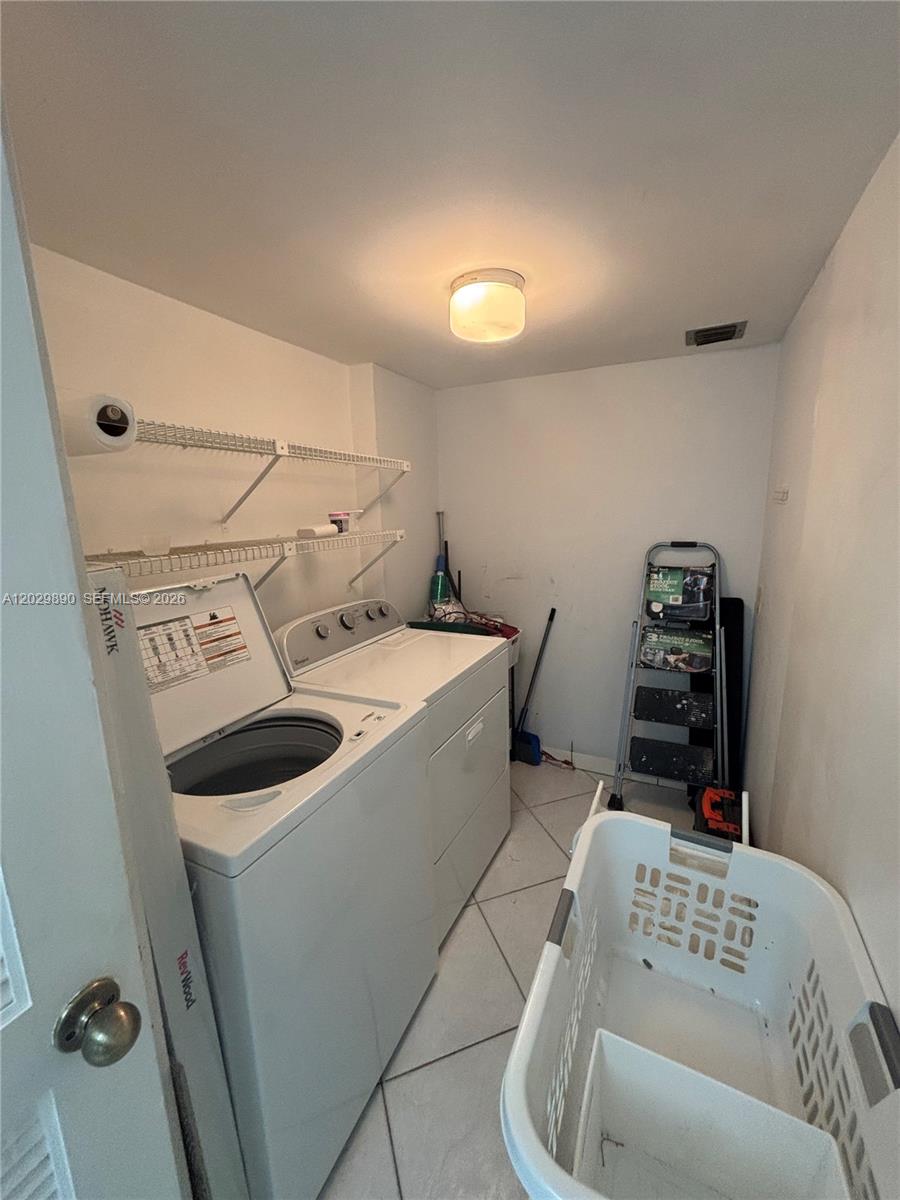 A laundry room features a white washer and dryer, wire shelving, and tile flooring — TAMARAC, FL