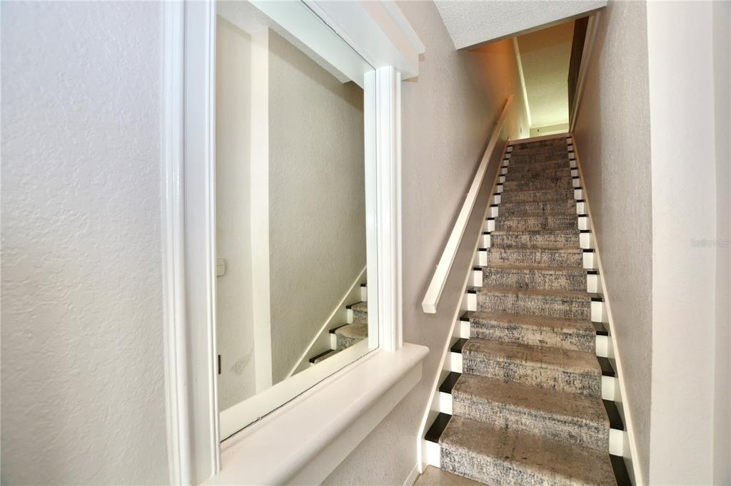 A staircase with patterned carpet and black-and-white trim sits beside a wall-mounted mirror — 858 NORMANDY TRACE ROAD, TAMPA, FL