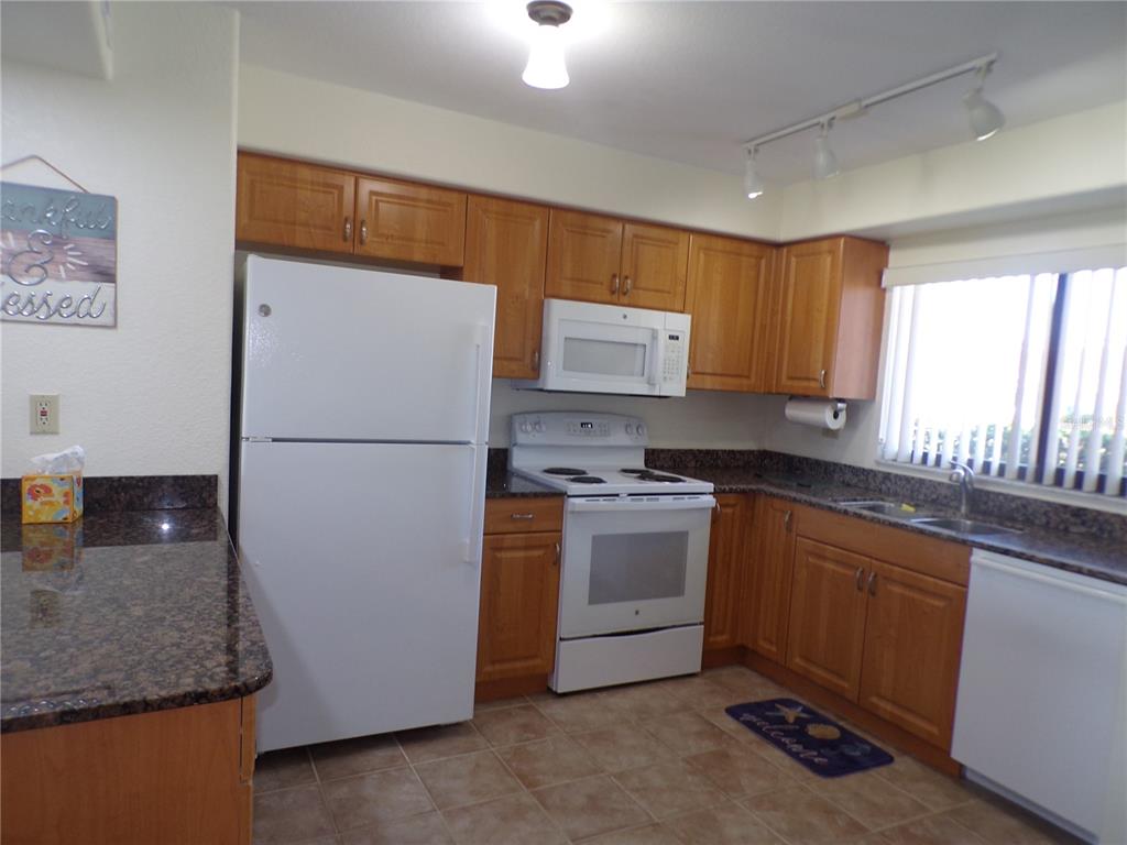 A kitchen features wood cabinets, granite countertops, white appliances, and tile flooring — 1356 RIO DE JANEIRO AVENUE UNIT 108, PUNTA GORDA, FL