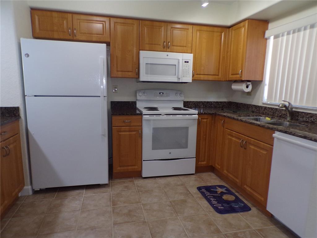 A kitchen features wood cabinets, granite countertops, white appliances, and light-colored tile flooring — 1356 RIO DE JANEIRO AVENUE UNIT 108, PUNTA GORDA, FL