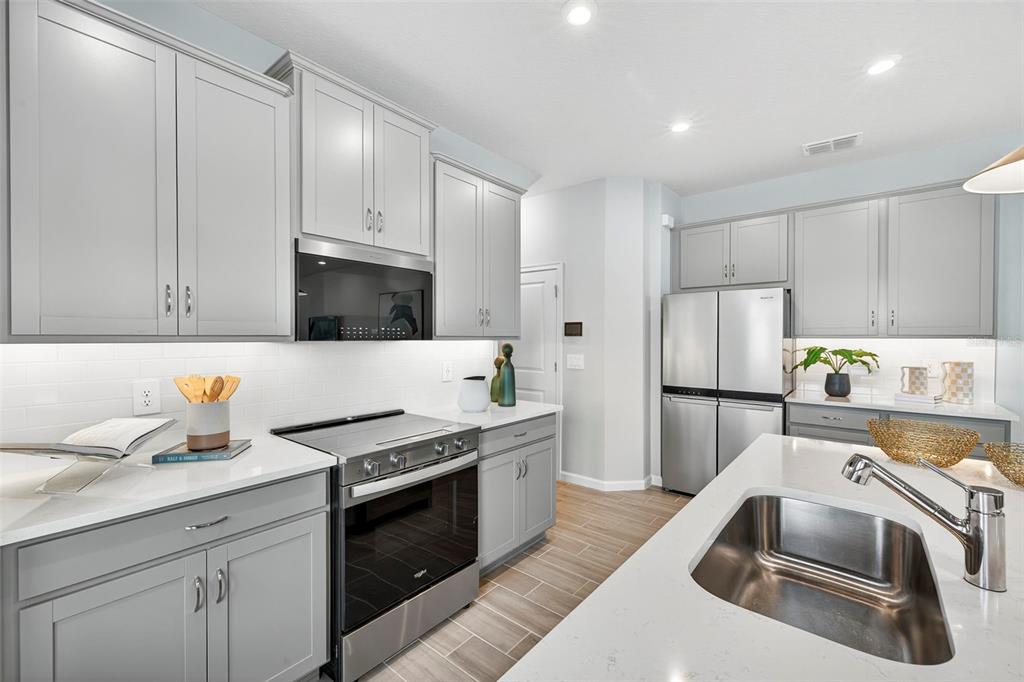 A modern kitchen features gray cabinets, stainless steel appliances, white countertops, and a center island — 8831 GINKO RUN, PARRISH, FL