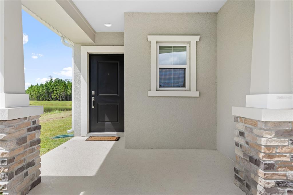 A covered front porch features a black door, a single window, and stone-accented columns — 1243 SAND TRAP COURT, DAYTONA BEACH, FL