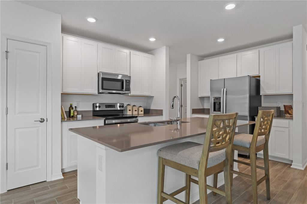 A modern kitchen features white cabinets, stainless steel appliances, and a central island with seating — 1243 SAND TRAP COURT, DAYTONA BEACH, FL