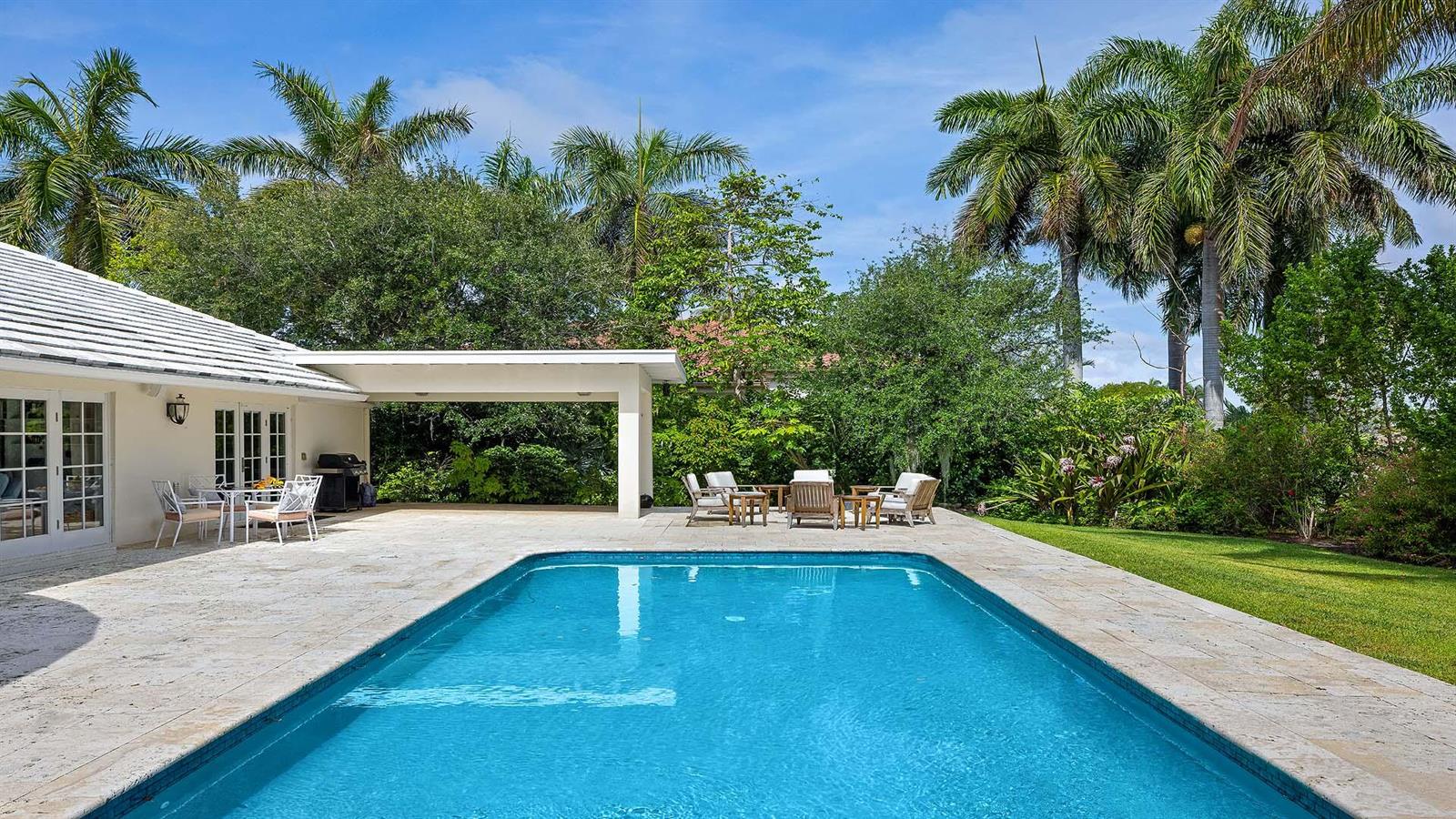 A rectangular swimming pool sits on a stone patio next to a house with palm trees — 335 Old School Road, Gulf Stream FL 33483, GULF STREAM, FL
