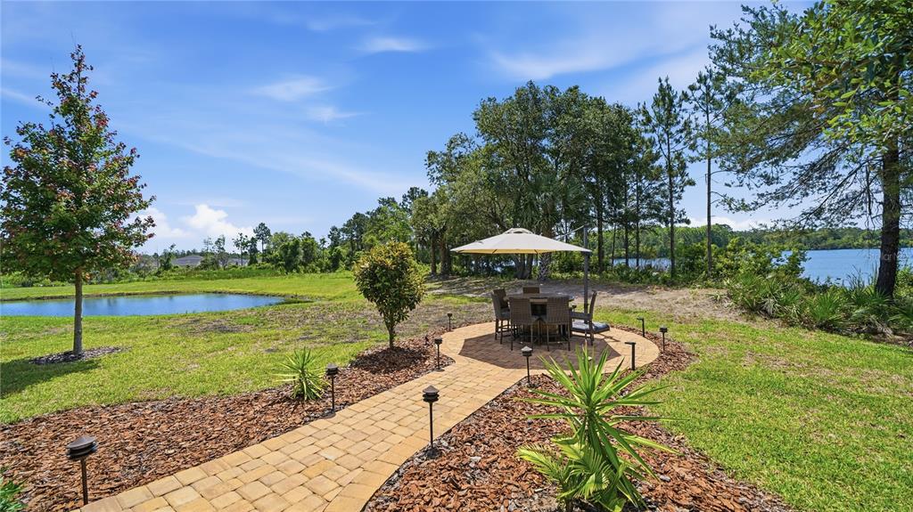 A paved walkway leads to a patio with a dining set under an umbrella by water — 367 LAKE SINCLAIR STREET, ST AUGUSTINE, FL