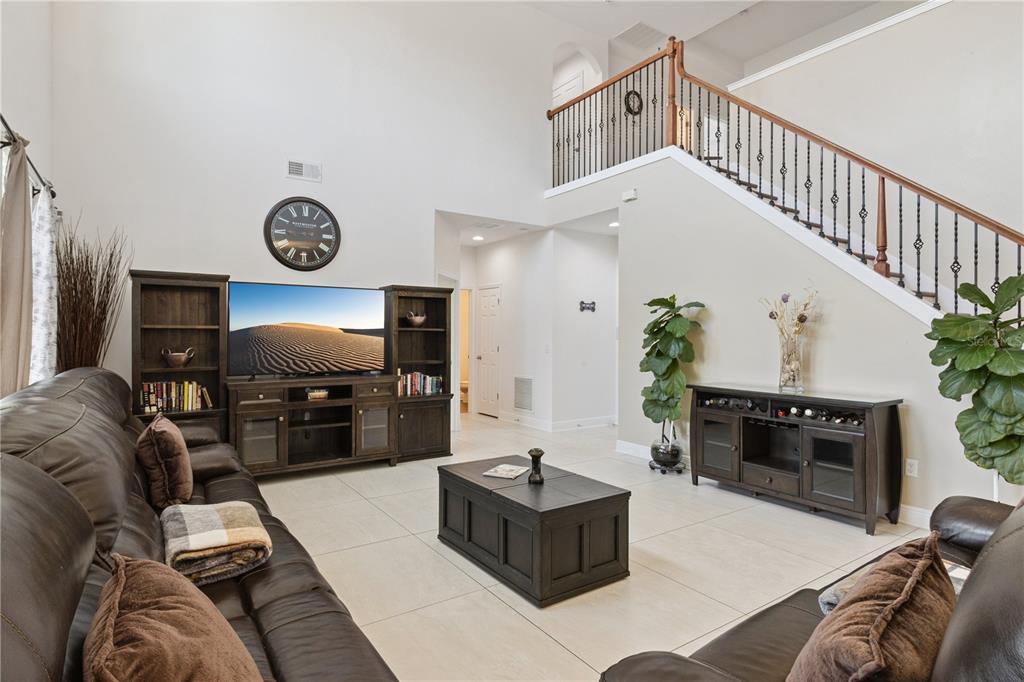 A living room features a high ceiling, a staircase with iron railings, and dark furniture — 3979 SUNSET LAKE DRIVE, LAKELAND, FL