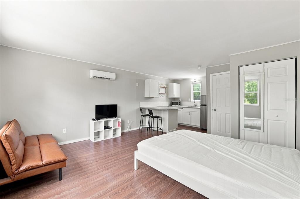 A studio apartment featuring a bed, a brown sofa, a kitchenette, and wood-look flooring — 6027 1ST AVENUE N UNIT B, ST PETERSBURG, FL