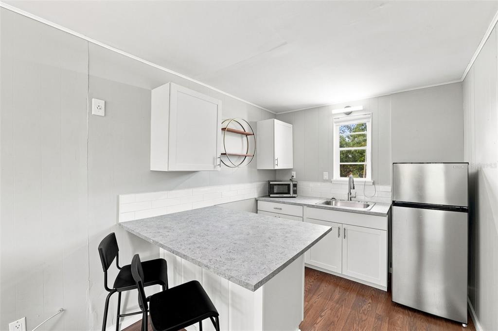 A kitchen with white cabinets, a gray countertop island, stainless steel refrigerator, and wood flooring — 6027 1ST AVENUE N UNIT B, ST PETERSBURG, FL