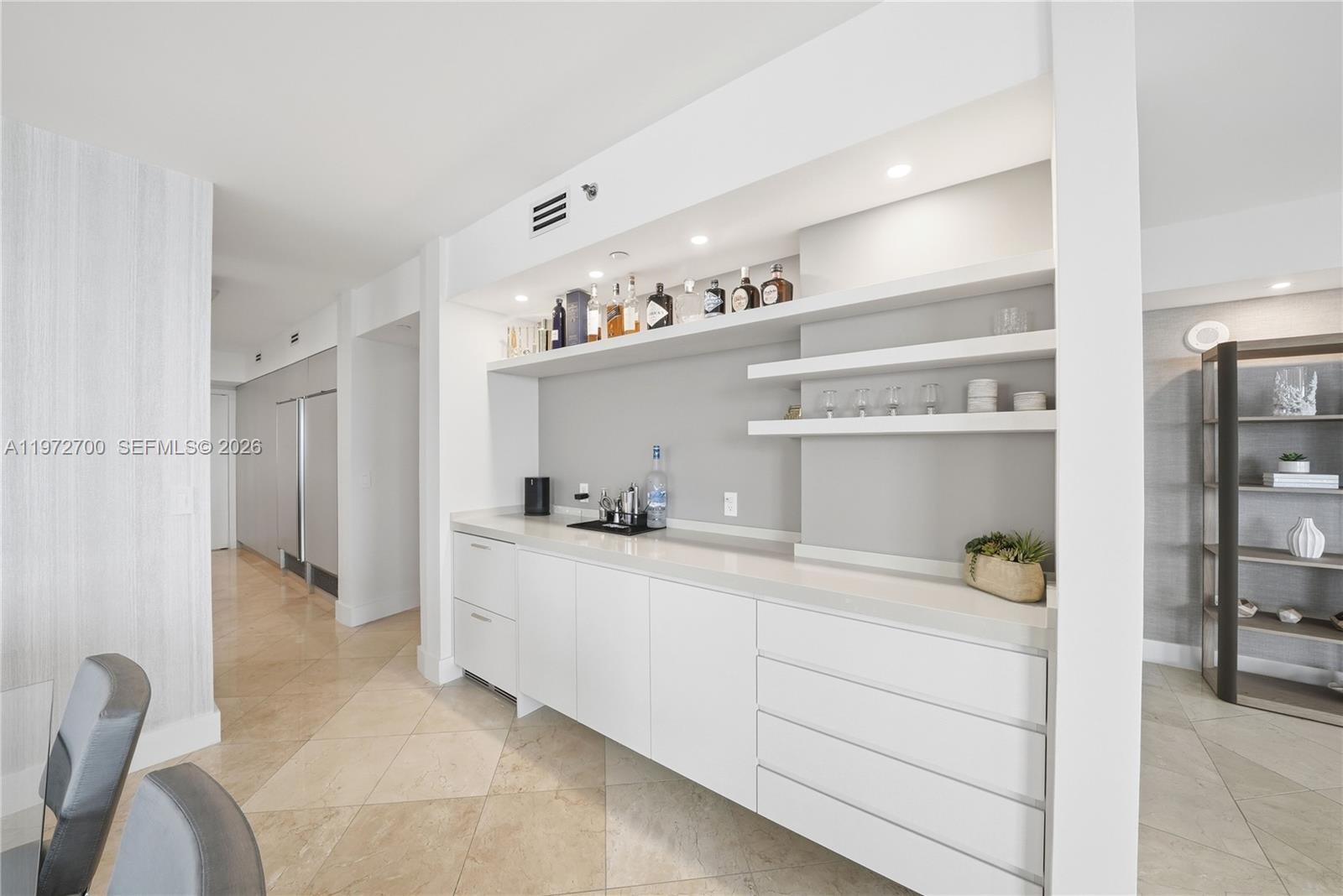 A modern white wet bar features open shelving, recessed lighting, and a stone countertop — 5801 Collins Ave # 700, Miami Beach FL 33140, MIAMI BEACH, FL