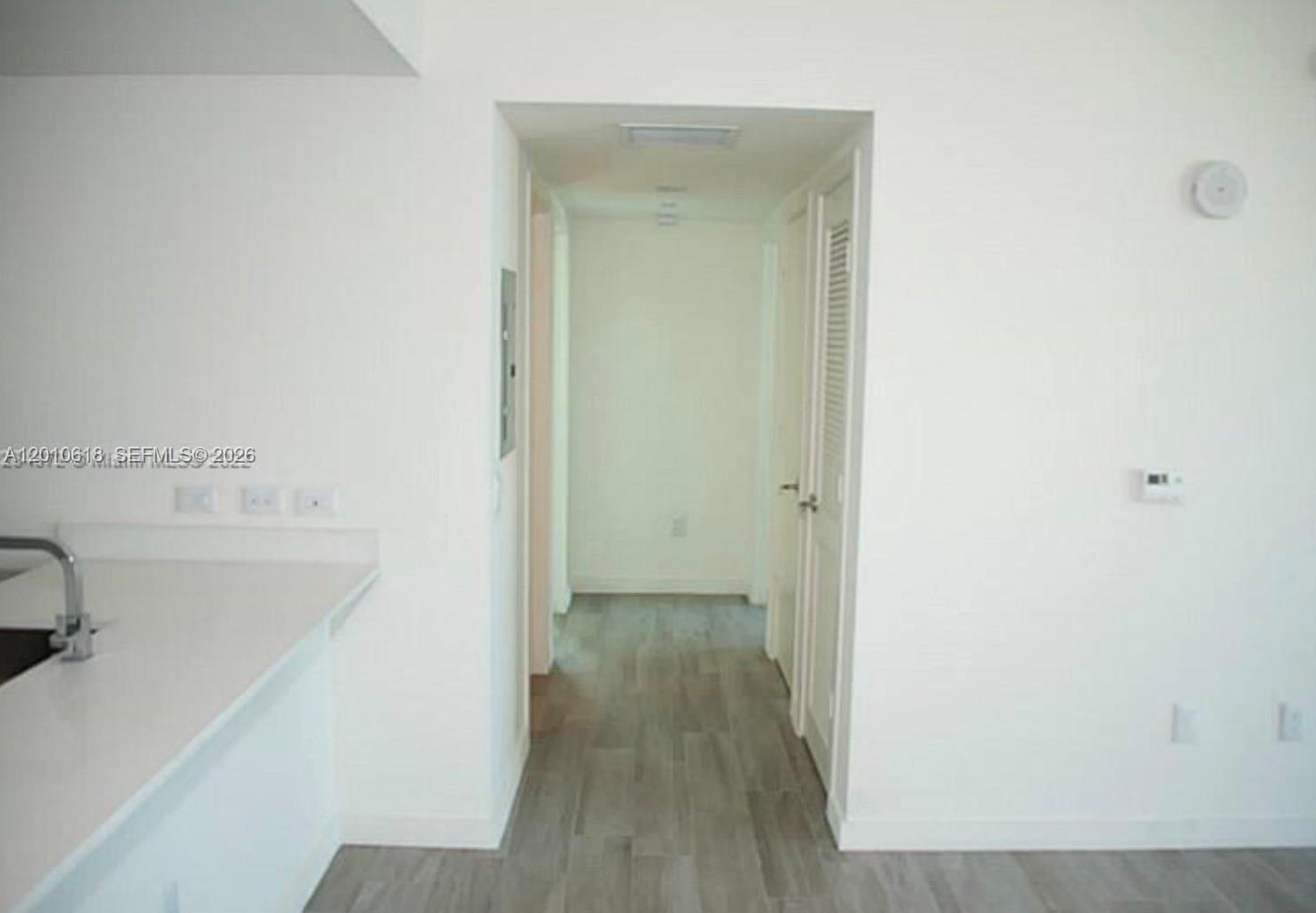 A hallway with light wood-look flooring leads from a kitchen area toward a doorway — 1100 S Miami Ave # 2407, Miami FL 33130, MIAMI, FL