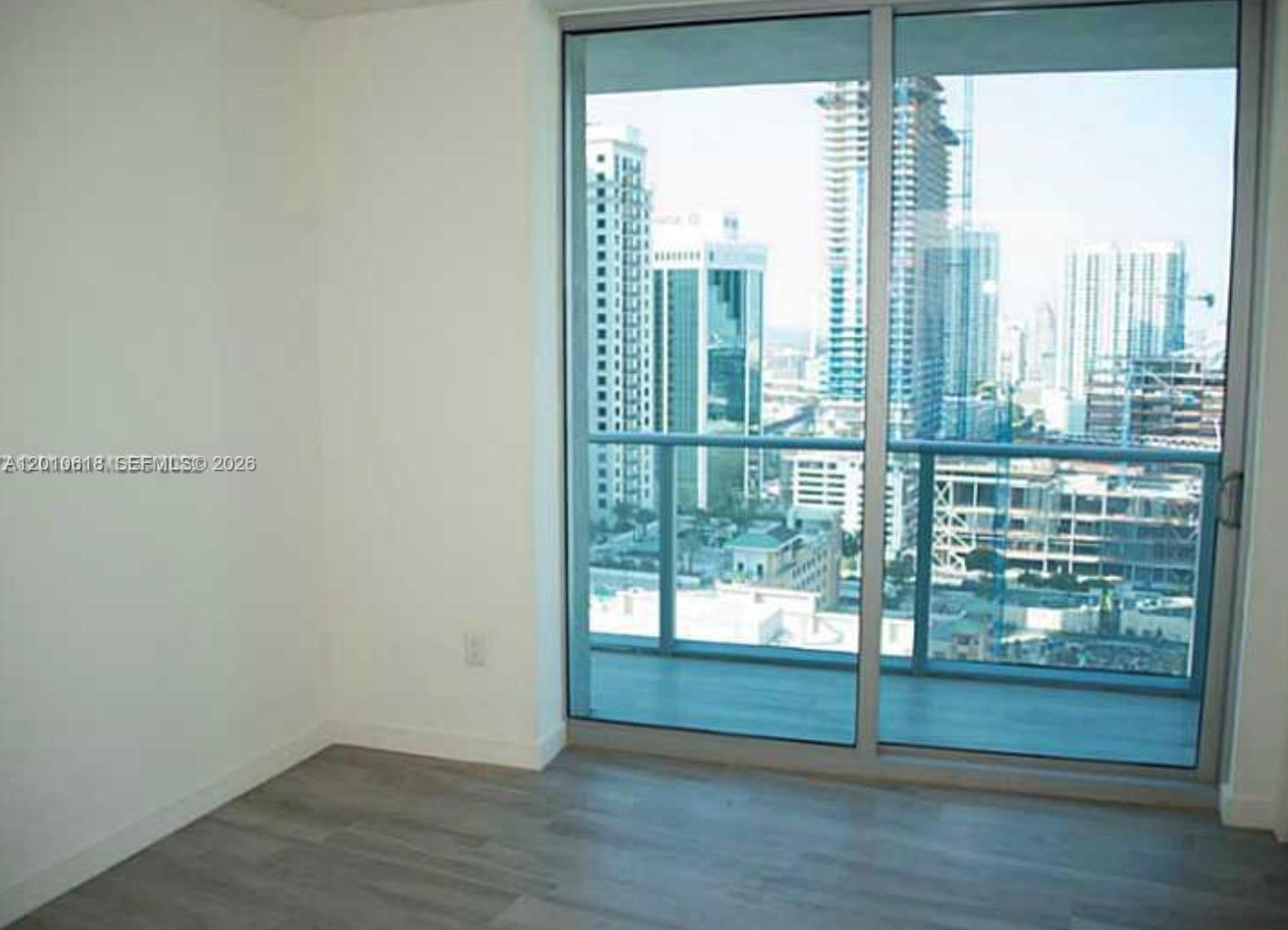 An empty room features light wood-look flooring, white walls, and a large glass balcony door — 1100 S Miami Ave # 2407, Miami FL 33130, MIAMI, FL