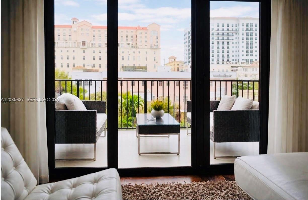 A balcony with outdoor furniture is visible through large glass doors from a living room — 100 Andalusia Ave # 402, Coral Gables FL 33134, CORAL GABLES, FL