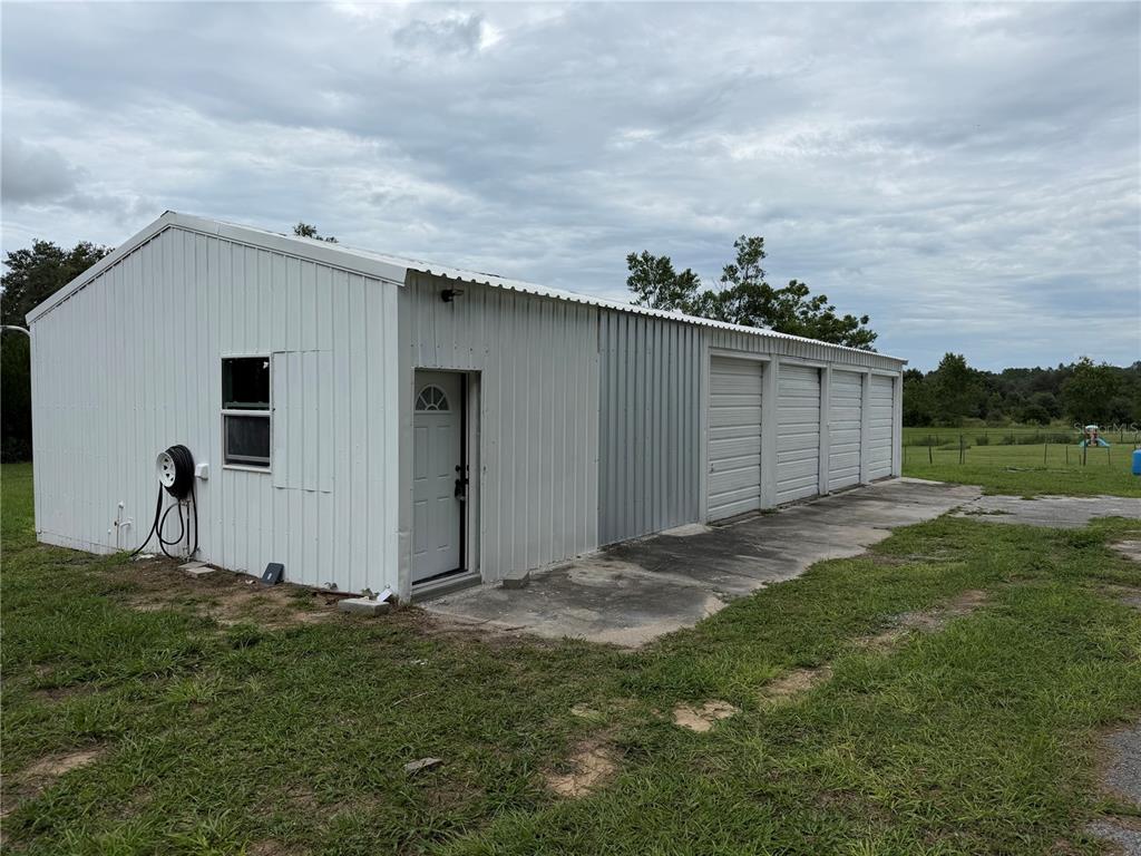 A white metal-sided garage building with a single entry door and three roll-up doors — 37631 KOSSIK ROAD, ZEPHYRHILLS, FL