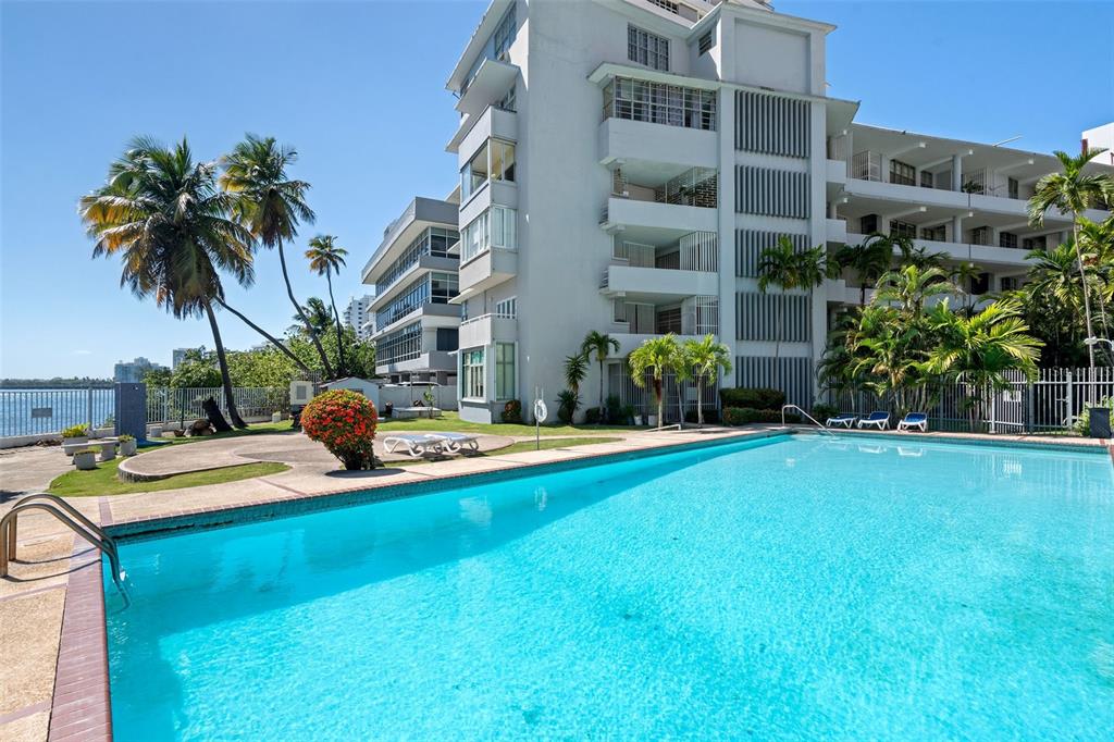 A swimming pool sits in front of a multi-story apartment building with palm trees — 1020 AVE. ASHFORD UNIT 302, SAN JUAN, PR