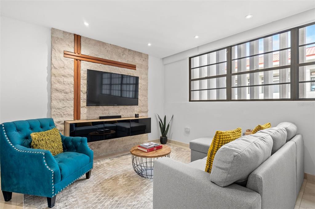 A living room features a stone accent wall with a mounted television and a blue armchair — 1020 AVE. ASHFORD UNIT 302, SAN JUAN, PR