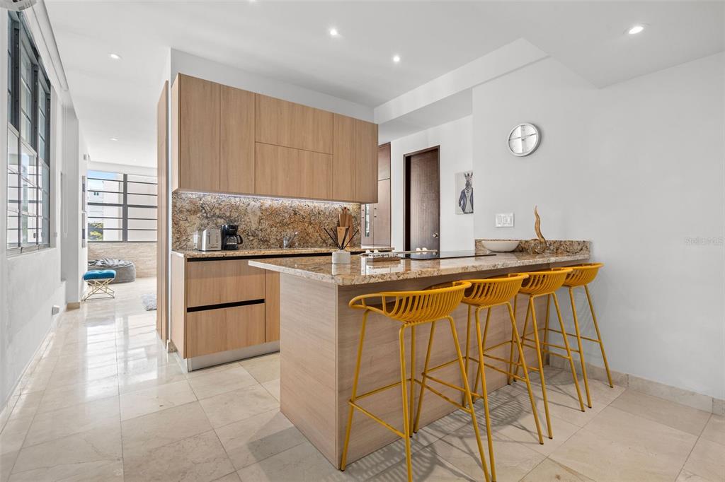 A modern kitchen features light wood cabinets, granite countertops, and three yellow bar stools — 1020 AVE. ASHFORD UNIT 302, SAN JUAN, PR