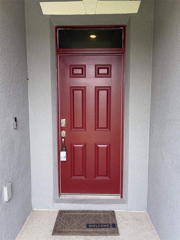 A red front door with a transom window and a welcome mat in a recessed entryway — 6799 SARUS CRANE POINT, ST CLOUD, FL