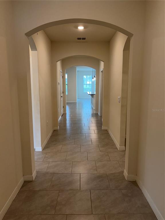 A long hallway with arched entryways and light-colored tile flooring leads toward an open living area — 6799 SARUS CRANE POINT, ST CLOUD, FL