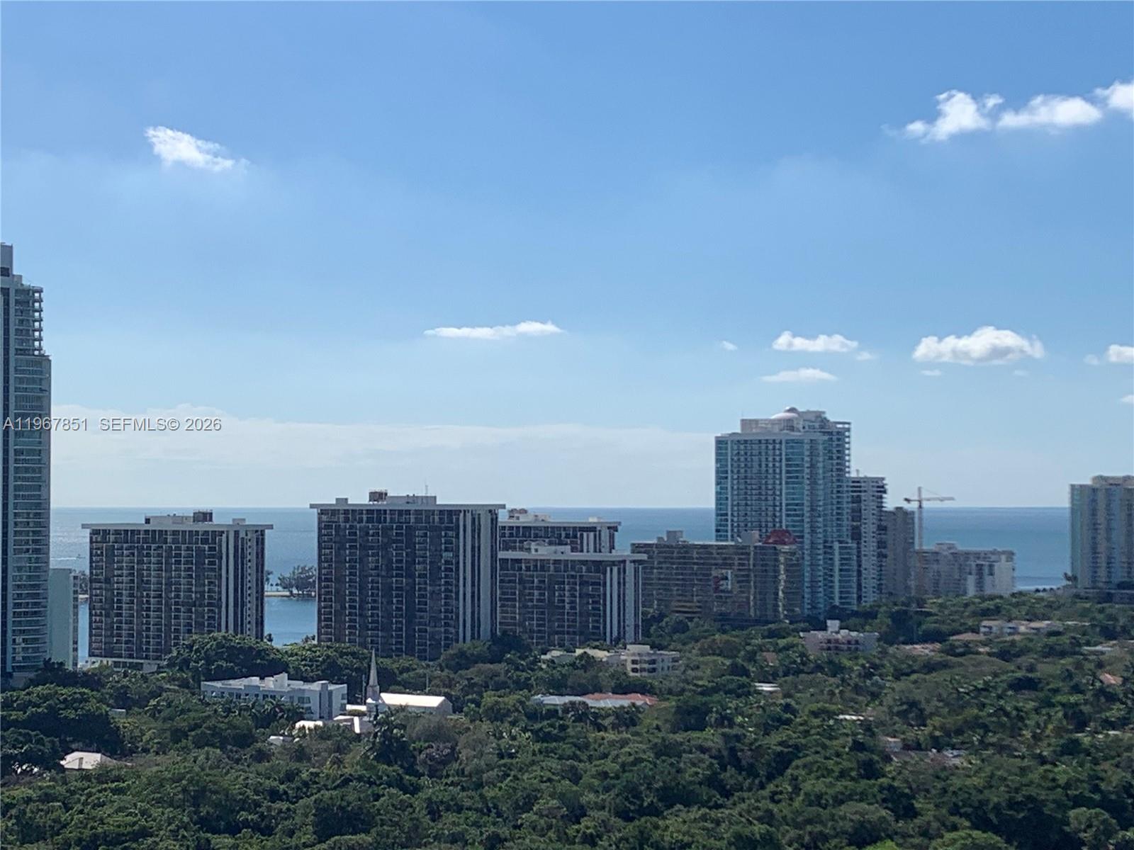 An elevated view shows several high-rise apartment buildings surrounded by trees near the ocean — 79 SW 12th St, Miami FL 33130, MIAMI, FL