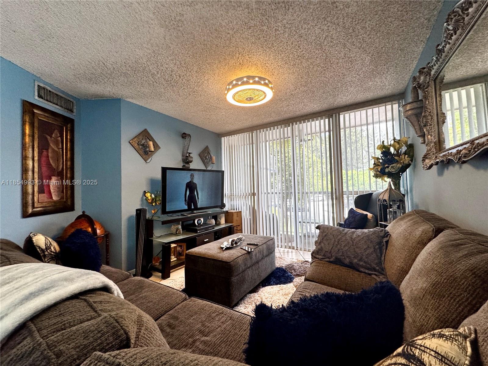 A living room features a sectional sofa, a television, and a ceiling fan light fixture — 7165 NW 186th St # A211, Hialeah FL 33015, HIALEAH, FL