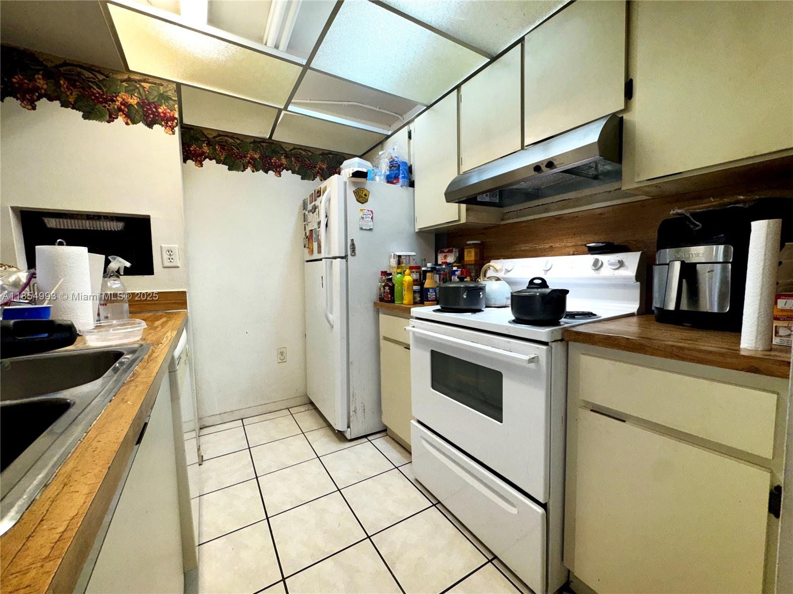 A galley kitchen features white appliances, light-colored cabinetry, wood-look countertops, and a drop ceiling — 7165 NW 186th St # A211, Hialeah FL 33015, HIALEAH, FL