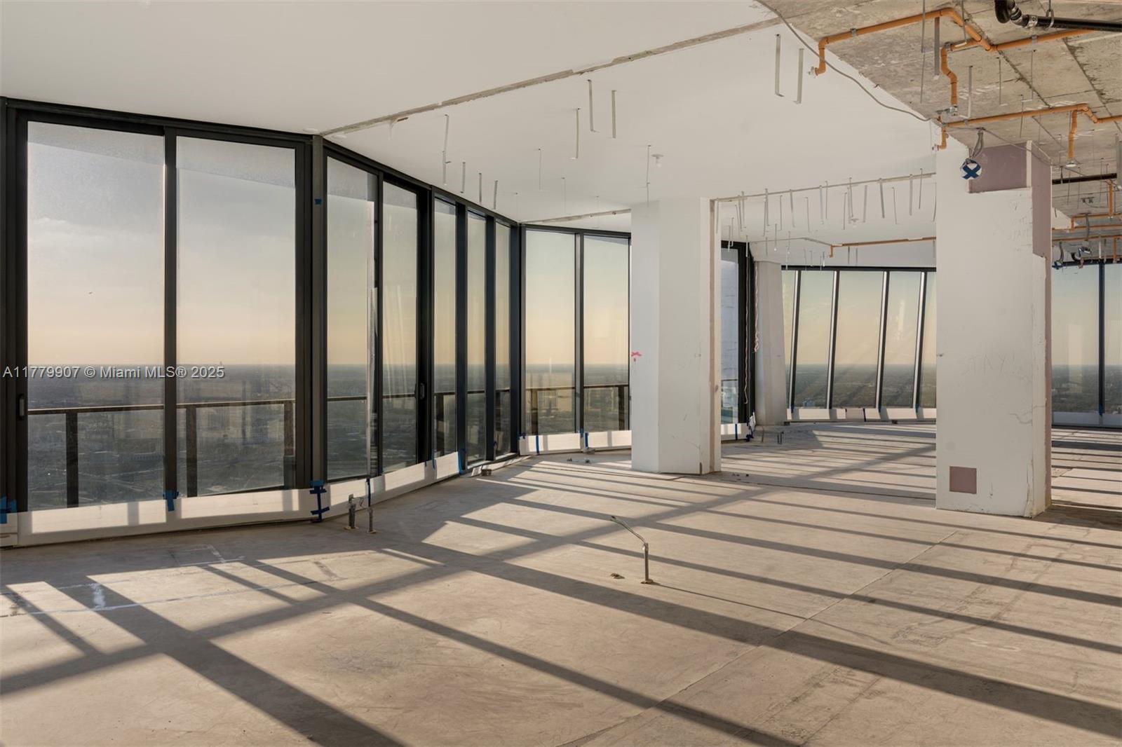 An unfinished high-rise interior features floor-to-ceiling windows, exposed concrete ceilings, and panoramic city views — 1000 Biscayne Blvd # 5801, Miami FL 33132, MIAMI, FL