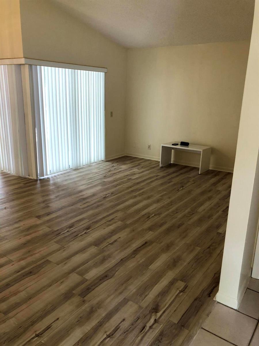 An empty room features light-colored walls, wood-look flooring, and a sliding glass door with blinds — 1371 Cottonwood Circle, Weston FL 33326, WESTON, FL