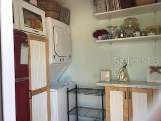 A laundry room features a stacked washer and dryer, open shelving, and wood-paneled cabinetry — 20285 US HIGHWAY 27 UNIT 21, CLERMONT, FL