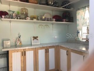 A kitchen features light wood cabinets with white panels, marble-look countertops, and open shelving — 20285 US HIGHWAY 27 UNIT 21, CLERMONT, FL