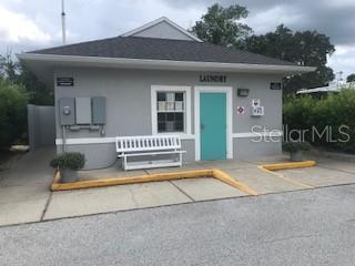A gray laundry building features a teal door, a white bench, and a shingled roof — 20285 US HIGHWAY 27 UNIT 21, CLERMONT, FL