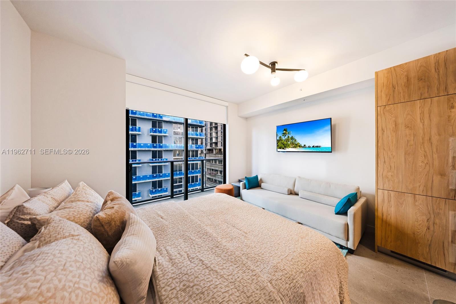 A bedroom features a bed, a sofa, a wall-mounted television, and a balcony view — 11 NE 6th St # 1208, Miami FL 33132, MIAMI, FL