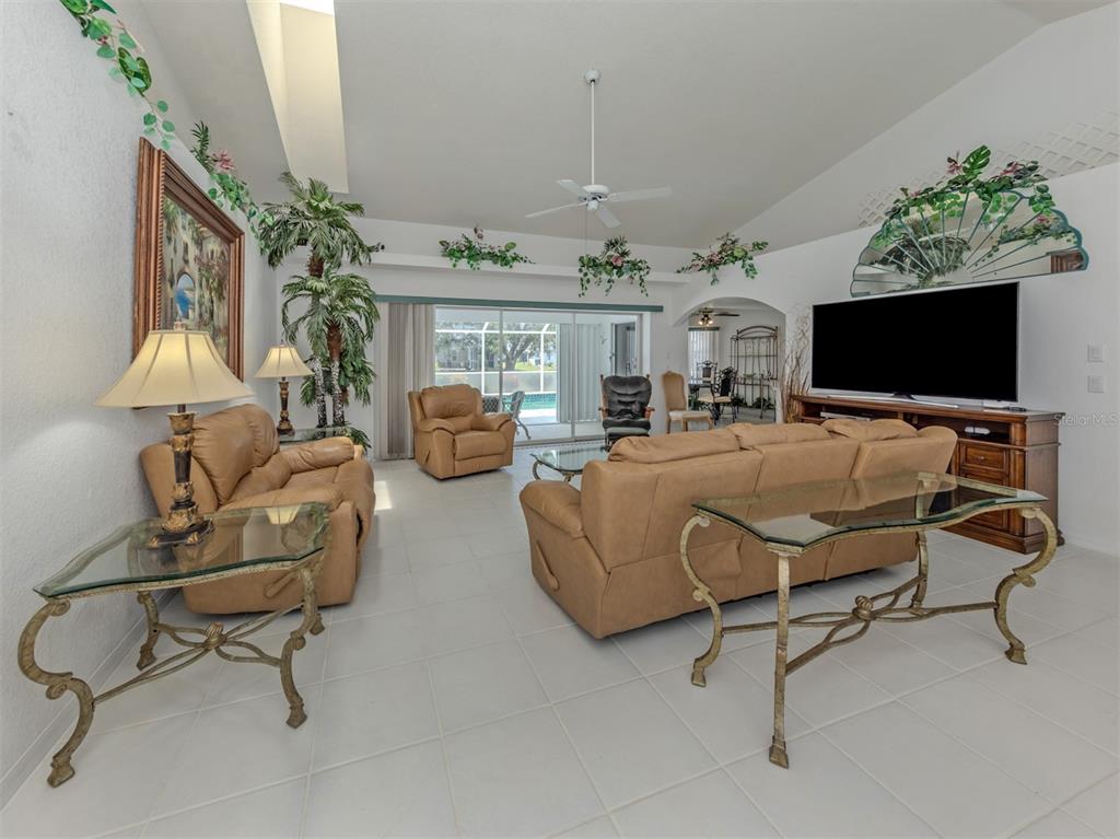 A living room features tan leather furniture, a glass-topped console table, and a large television — 25244 RAMPART BOULEVARD, PUNTA GORDA, FL