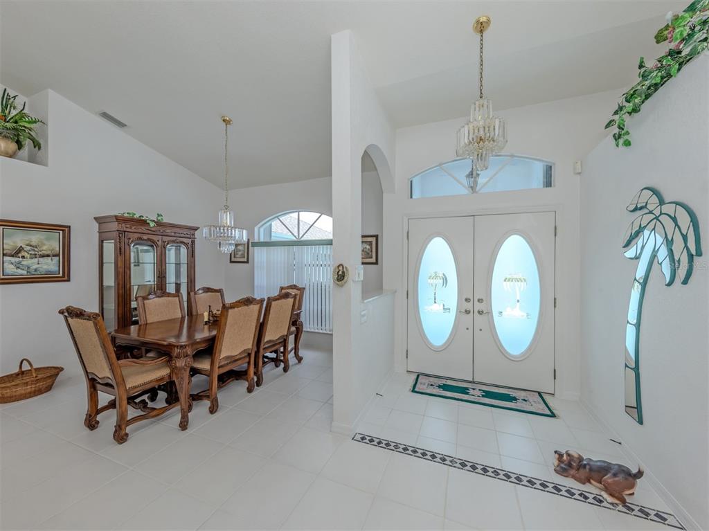 A dining room and entryway feature white tile floors, crystal chandeliers, and double front doors — 25244 RAMPART BOULEVARD, PUNTA GORDA, FL
