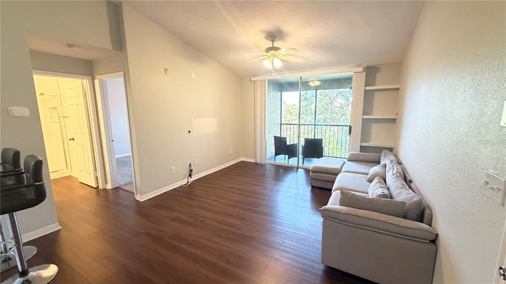 A living room features wood-look flooring, a gray sectional sofa, and a sliding glass balcony door — 8849 LATREC AVENUE UNIT 4202, ORLANDO, FL