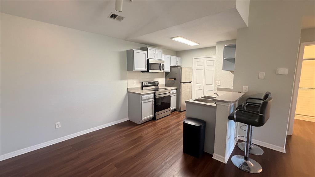 A kitchen features light gray cabinets, stainless steel appliances, and a breakfast bar with stools — 8849 LATREC AVENUE UNIT 4202, ORLANDO, FL
