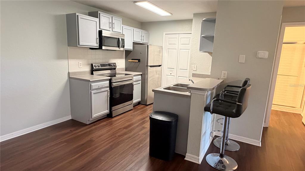 A kitchen features light gray cabinets, stainless steel appliances, a breakfast bar, and wood flooring — 8849 LATREC AVENUE UNIT 4202, ORLANDO, FL