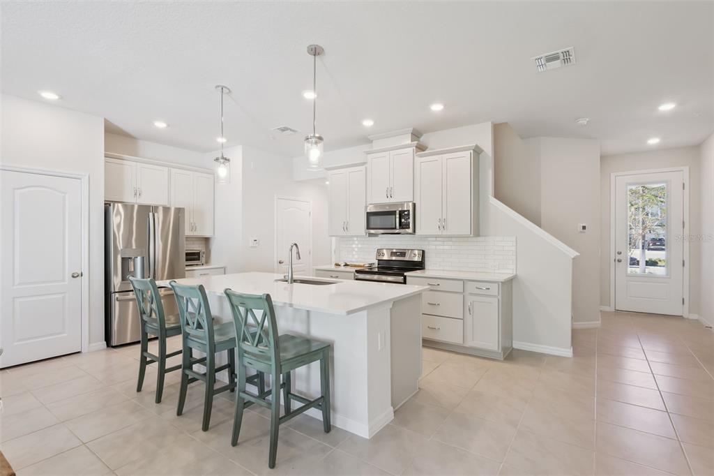 A modern kitchen features white cabinetry, a central island with bar seating, and tile flooring — 637 ASTERA WINDS LANE, LAKE MARY, FL