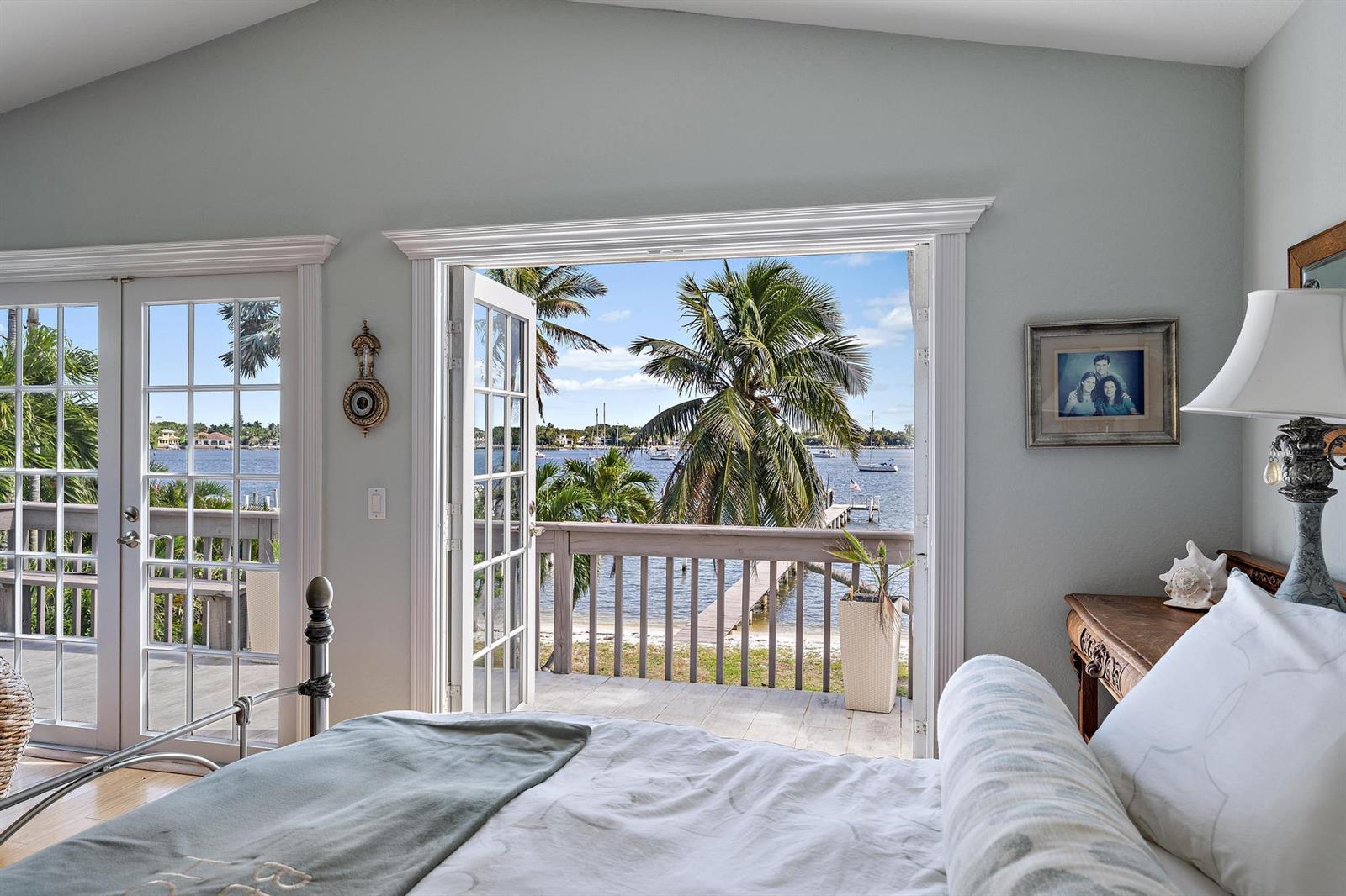 A bedroom with French doors opening to a deck overlooking a waterfront view with palm trees — 122 S Lake Drive, Lantana FL 33462, LANTANA, FL