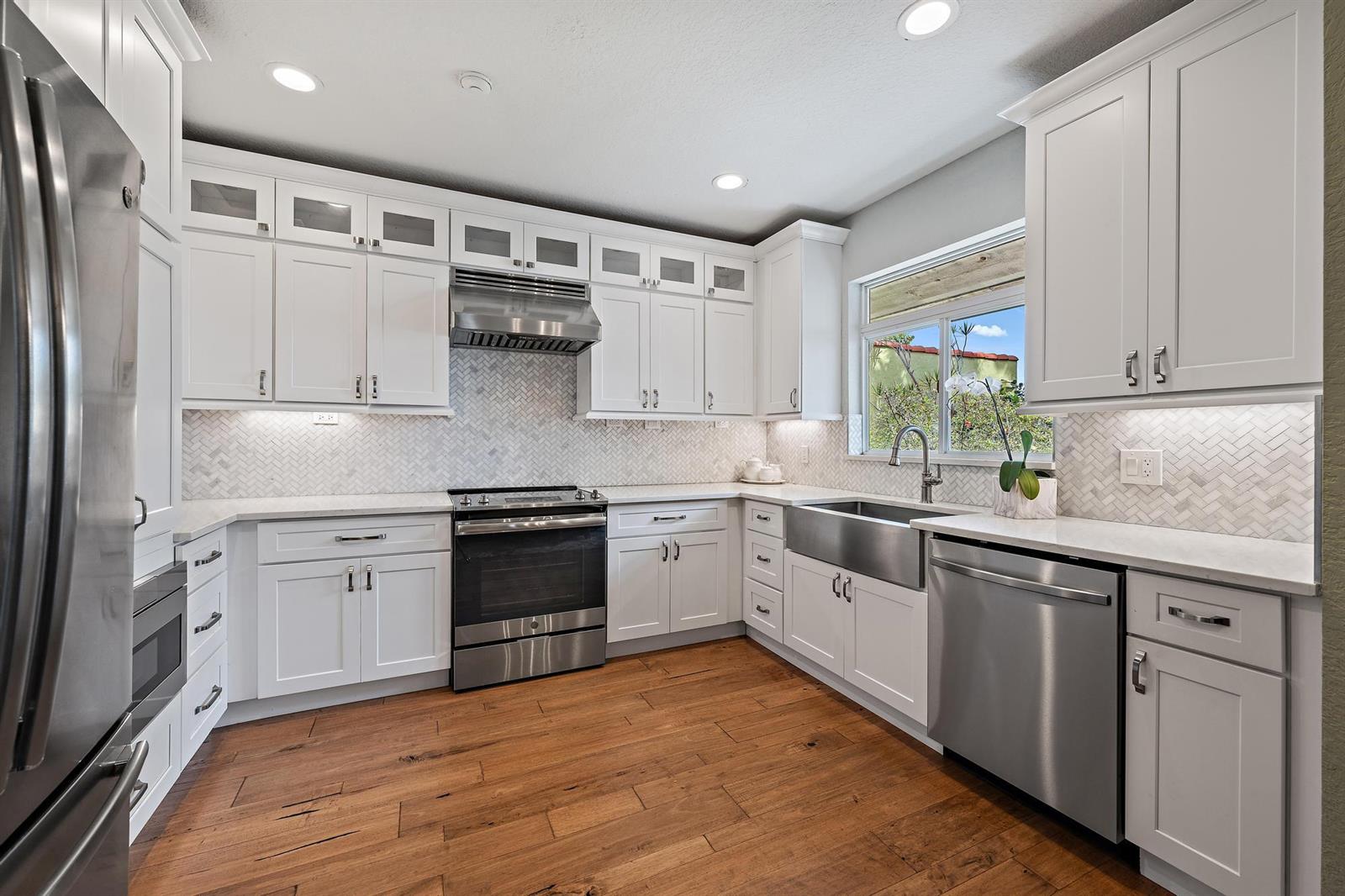 A kitchen with white cabinets, stainless steel appliances, a farmhouse sink, and wood-look flooring — 122 S Lake Drive, Lantana FL 33462, LANTANA, FL