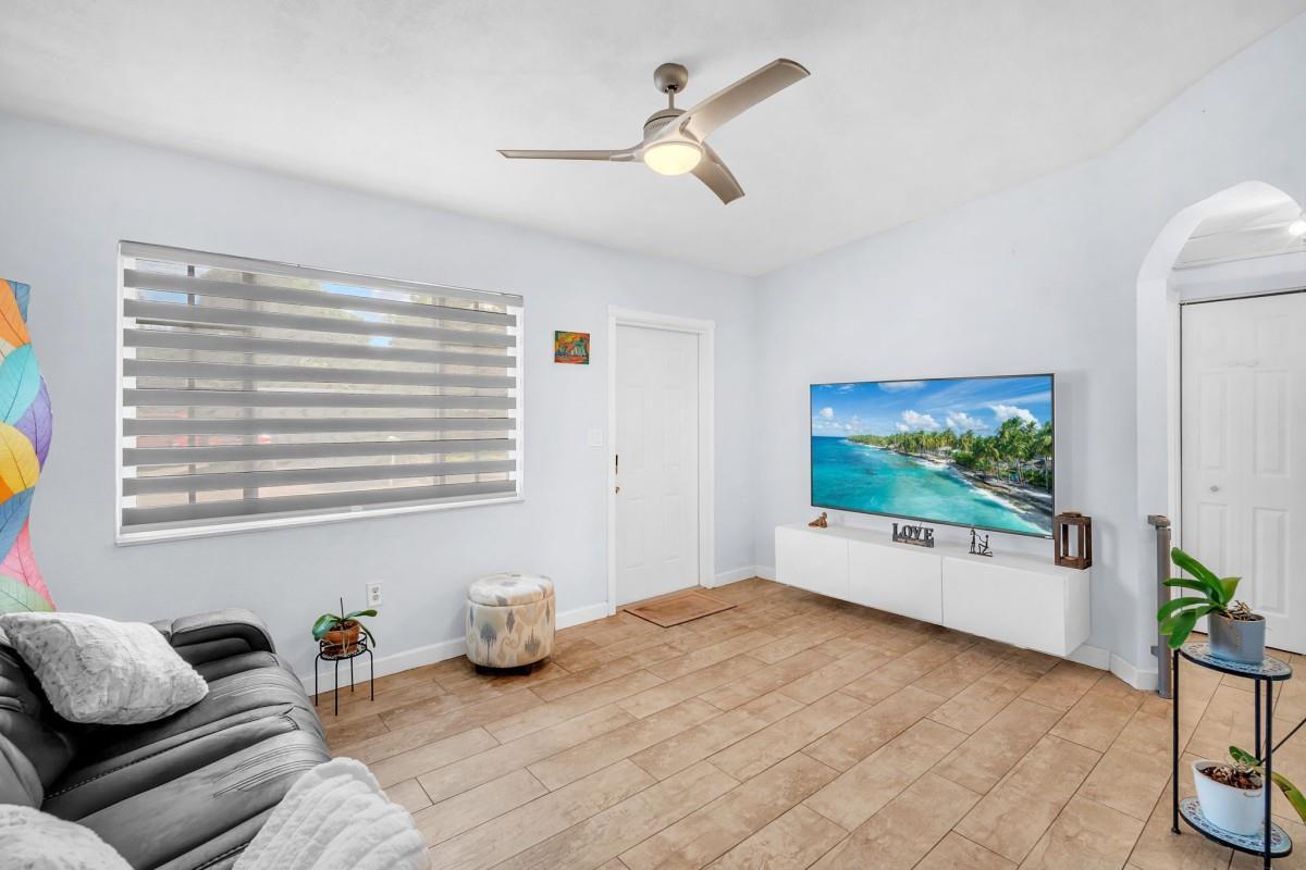 A living room features a wall-mounted television, a grey sofa, and tile flooring — 404 S 62nd Terrace, Hollywood FL 33023, HOLLYWOOD, FL