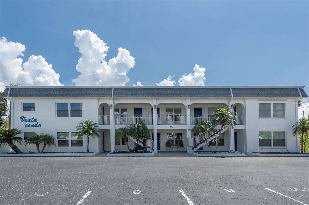 A two-story apartment building with white stucco walls, blue doors, and a parking lot — 7151 SUNSET WAY UNIT 3, ST PETE BEACH, FL