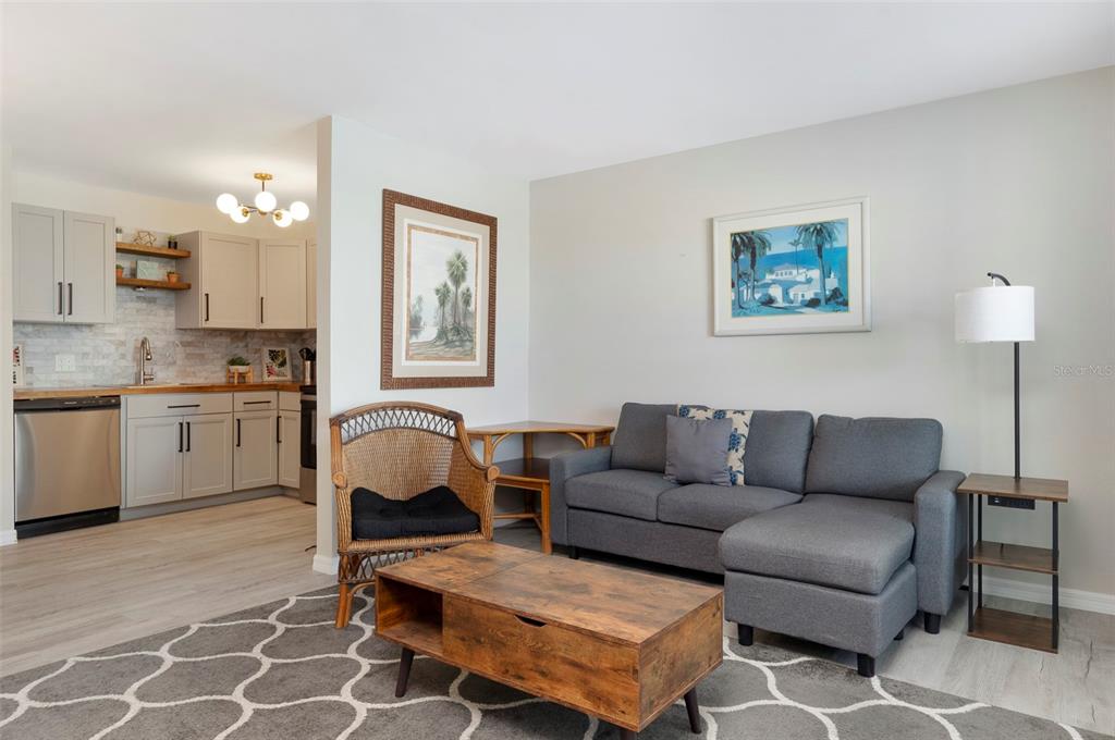 A living room with a grey sectional sofa, wicker chair, and an adjacent open kitchen — 7151 SUNSET WAY UNIT 3, ST PETE BEACH, FL