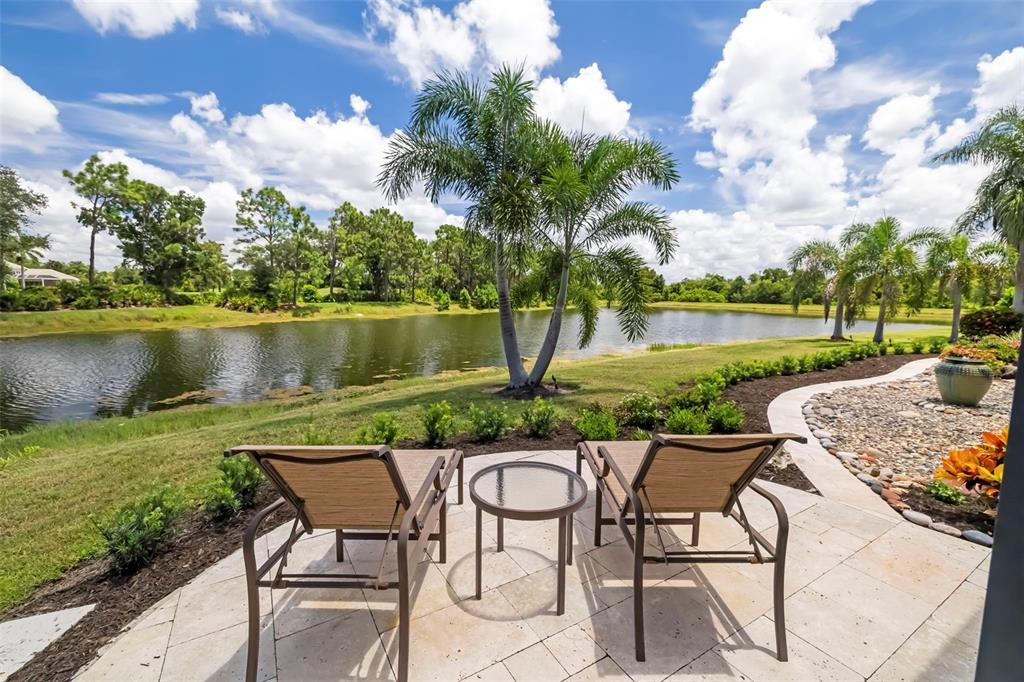 A patio with two lounge chairs and a small table overlooks a pond and trees — 7215 CHATSWORTH COURT, BRADENTON, FL