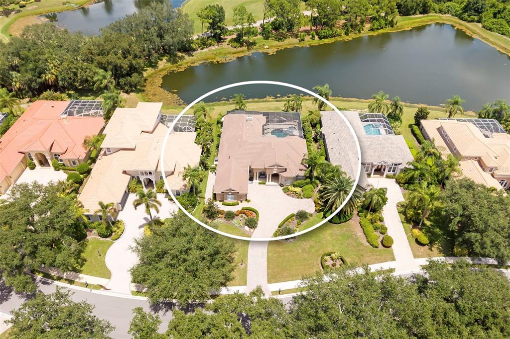 An aerial view shows a residential house with a pool enclosure near a lake — 7215 CHATSWORTH COURT, BRADENTON, FL
