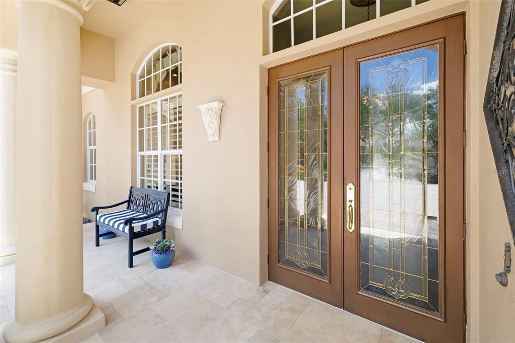 A covered entryway features a double glass door, a black bench, and a stone column — 7215 CHATSWORTH COURT, BRADENTON, FL