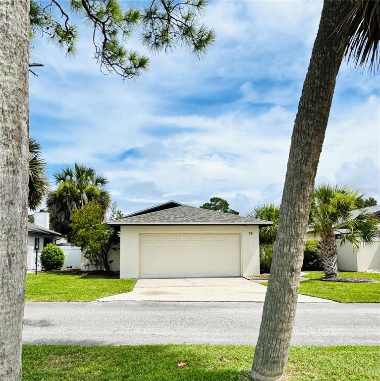 A single-story house exterior features a beige stucco facade, a two-car garage, and palm trees — 79 CLUB HOUSE DRIVE, PALM COAST, FL