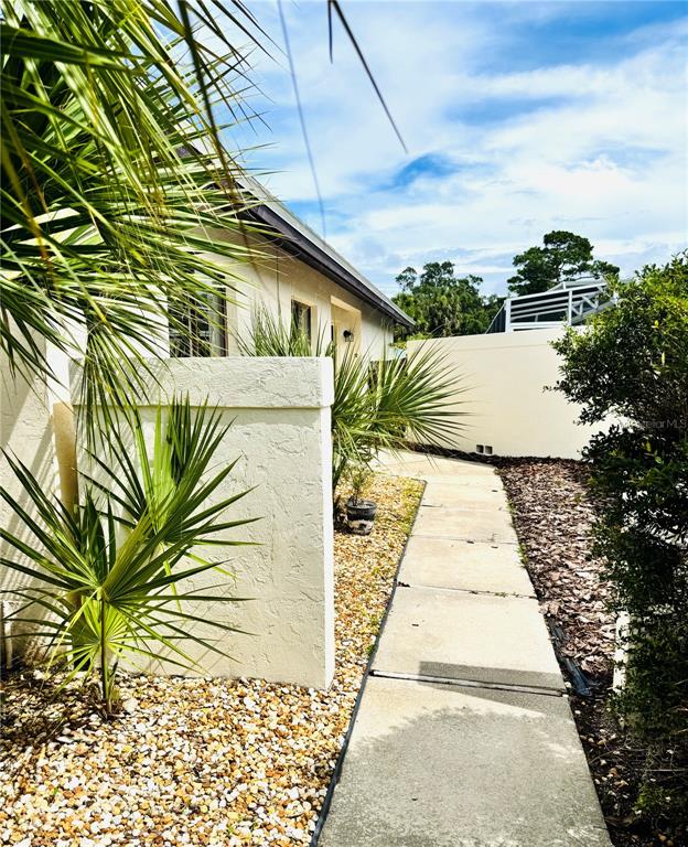 A concrete walkway leads past a stucco wall and palm plants toward a white fence — 79 CLUB HOUSE DRIVE, PALM COAST, FL